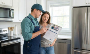 A professional licensed plumber discussing a detailed pricing estimate on a clipboard with a homeowner in a kitchen.