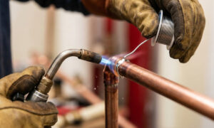 Close-up of a person safely soldering a residential copper pipe joint using a propane torch and lead-free solder.