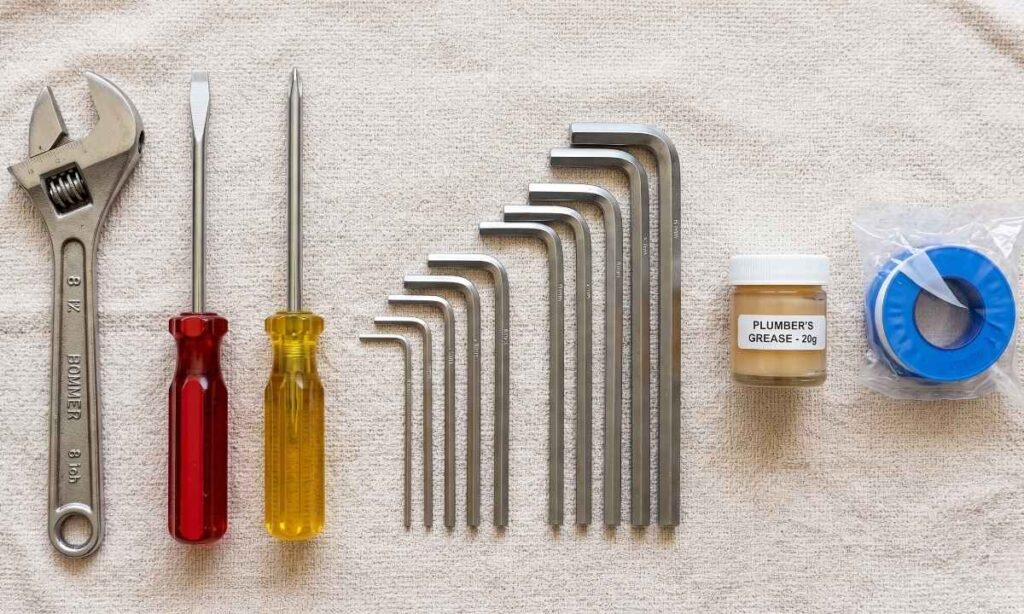 A collection of DIY plumbing supplies including an adjustable wrench, screwdrivers, and Teflon tape for faucet repair.