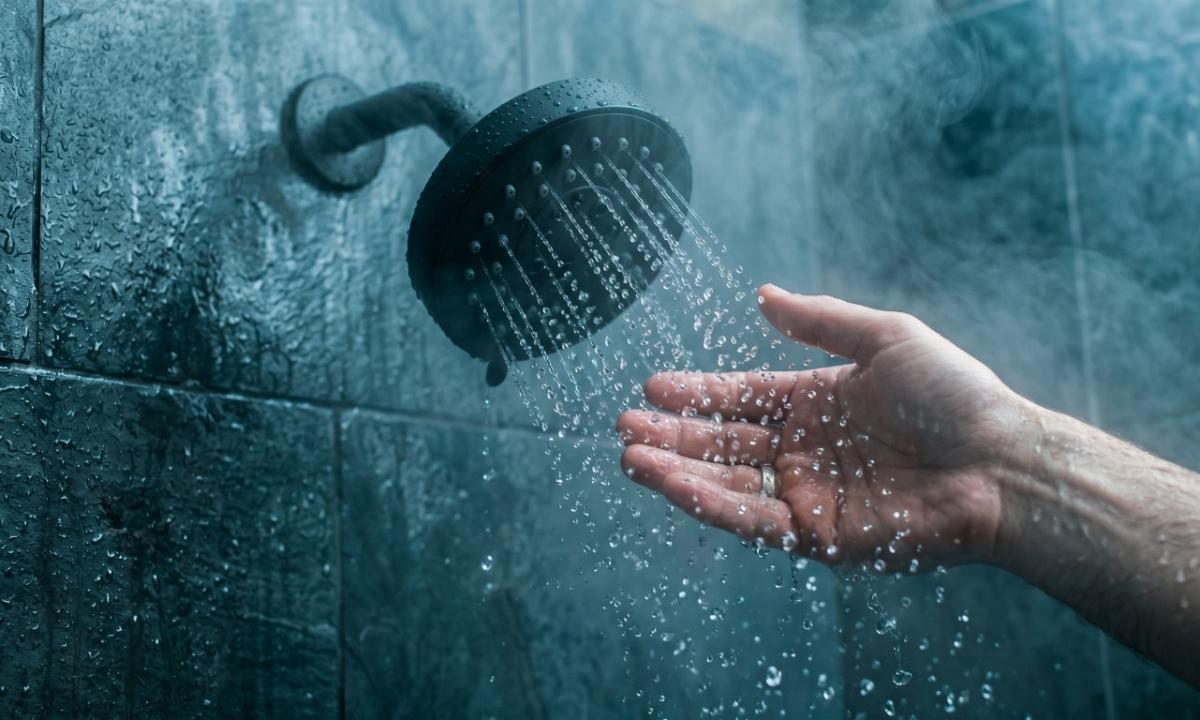 A hand testing water from a shower head to see why hot water runs out so fast.